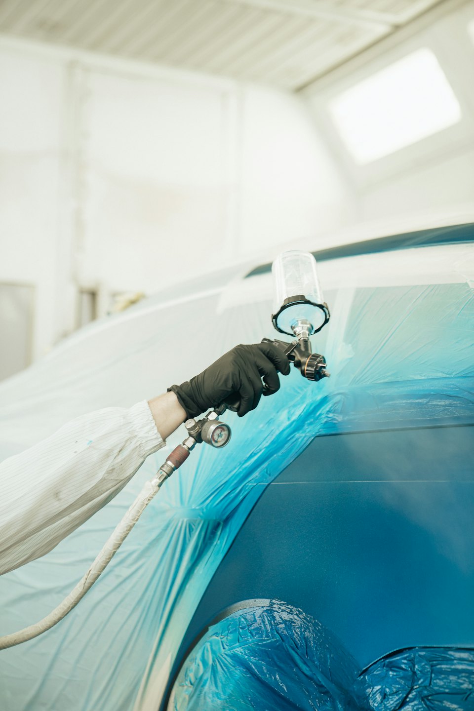 Maler in Schutzkleidung besprüht blaues Auto mit Spritzpistole.
