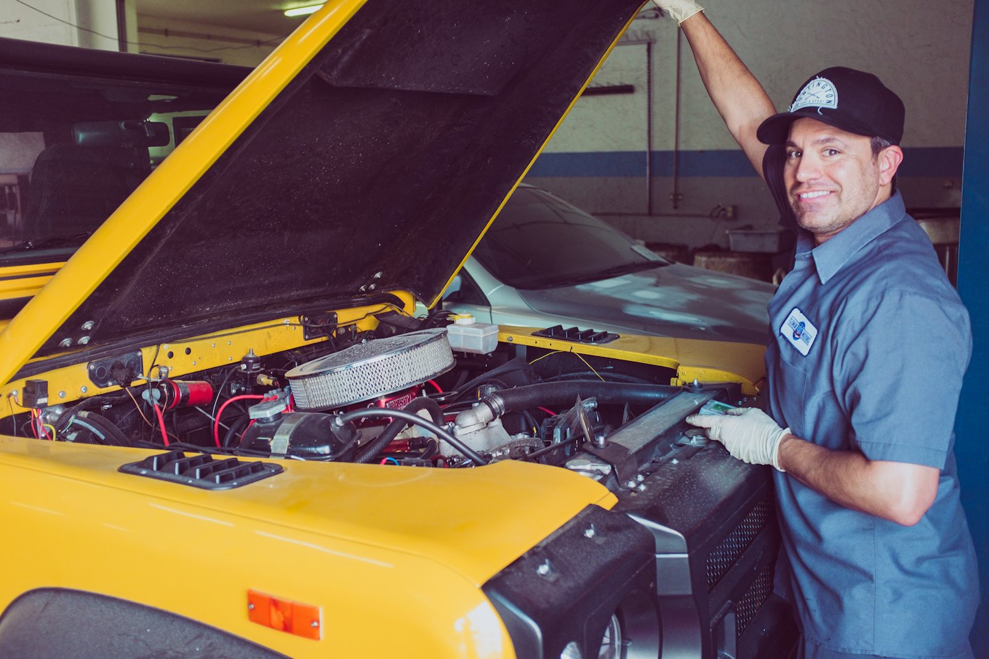 Lächelnder Mechaniker in blauer Uniform mit gelbem Auto.