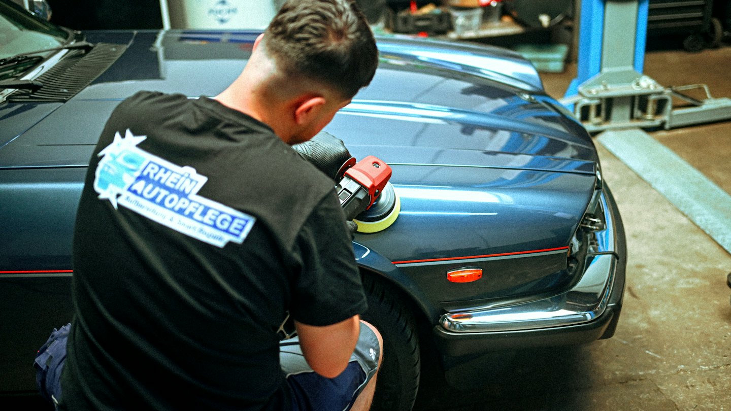 Professioneller Aufbereiter poliert einen dunkelblauen Oldtimer in einer Garage.