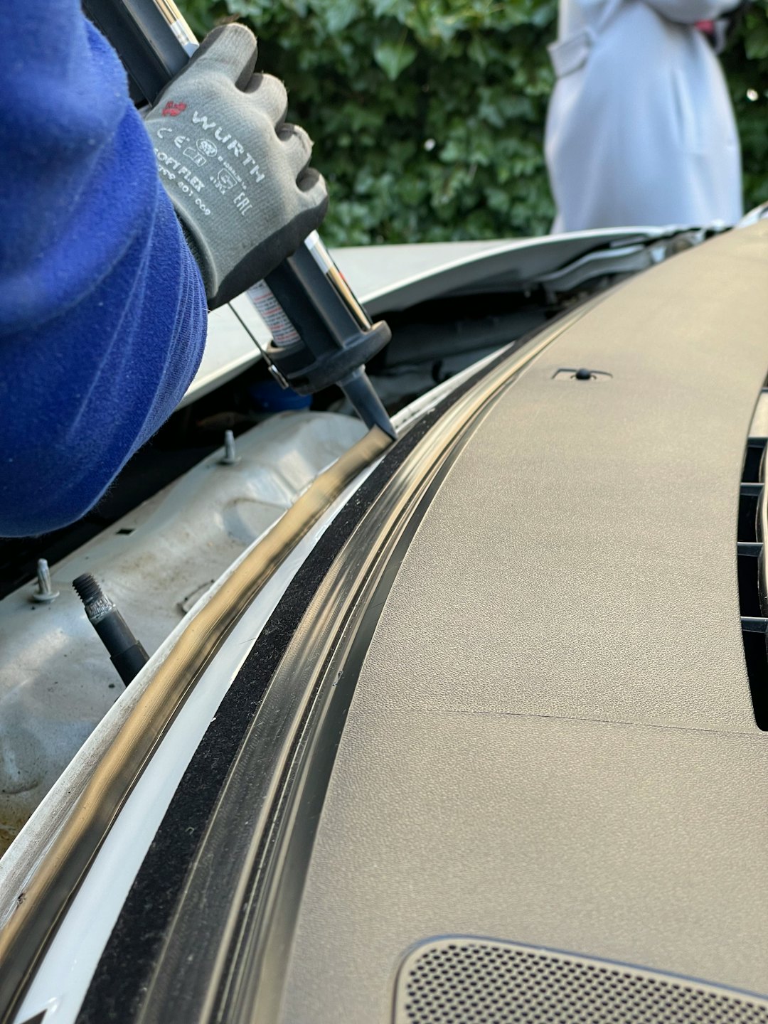 Mechaniker trägt Dichtmittel am Sockel einer Auto-Windschutzscheibe auf.